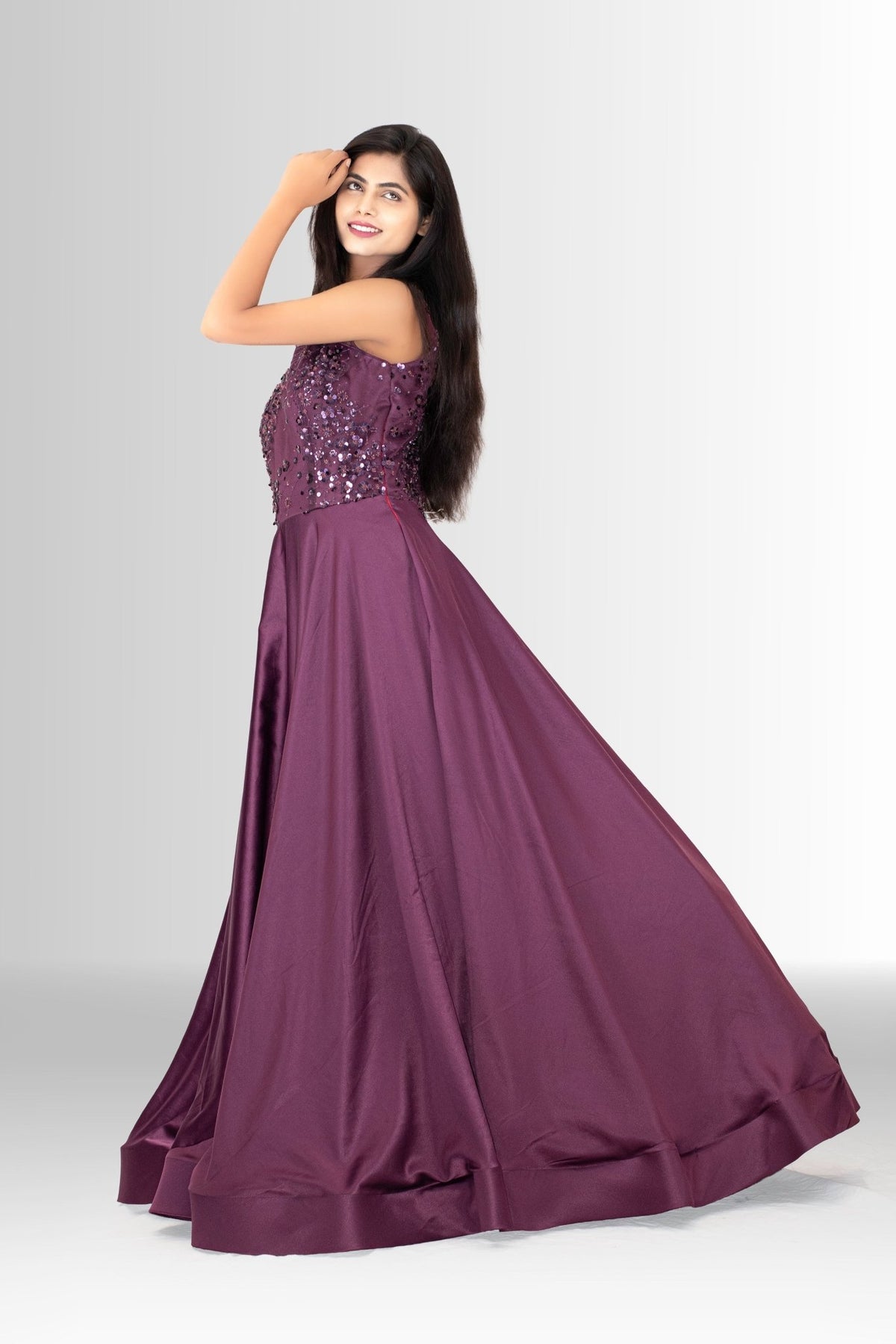 Woman smiling and posing in a designer party wear gown; the deep plum color contrasts with the sparkling sequins on the fitted top.