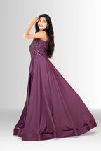 Woman smiling and posing in a designer party wear gown; the deep plum color contrasts with the sparkling sequins on the fitted top.