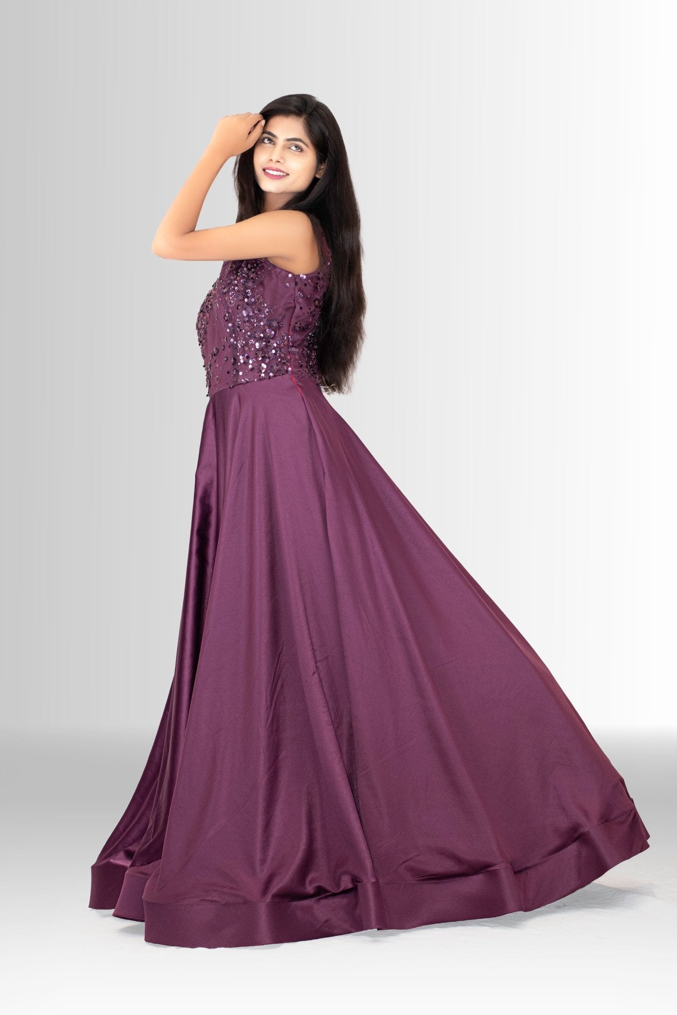 Woman smiling and posing in a designer party wear gown; the deep plum color contrasts with the sparkling sequins on the fitted top.