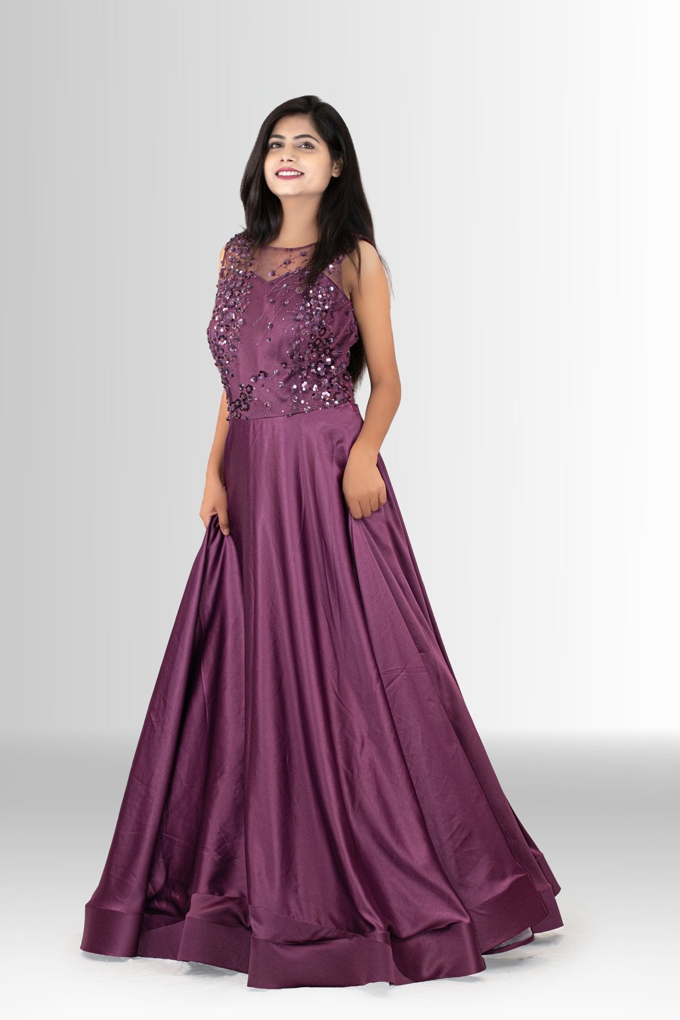 Woman smiling and posing in a designer party wear gown; the deep plum color contrasts with the sparkling sequins on the fitted top.