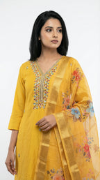 Woman wearing a yellow embroidered outfit with a floral pattern on a white background