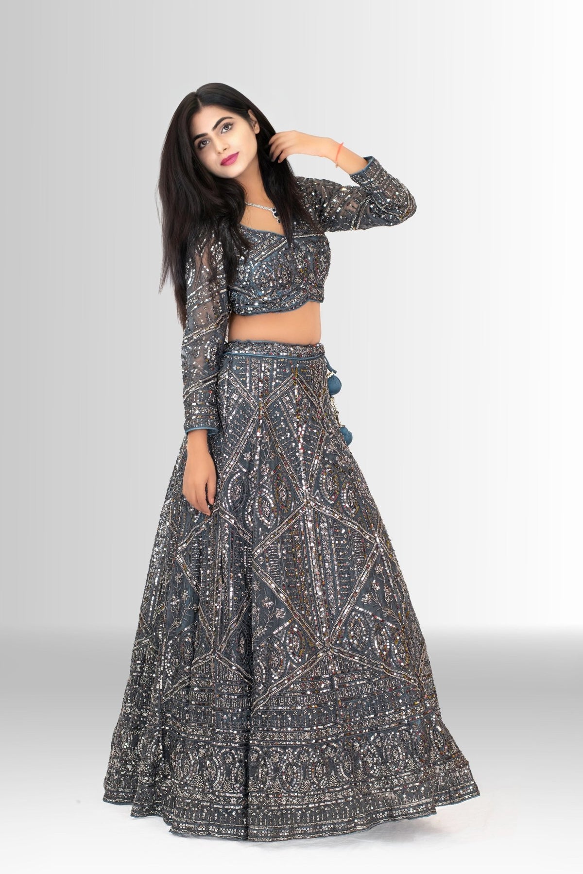 Model wearing a charcoal grey sequin lehenga choli by Rosio House, featuring a full-sleeve top and a sheer net dupatta with tassels.