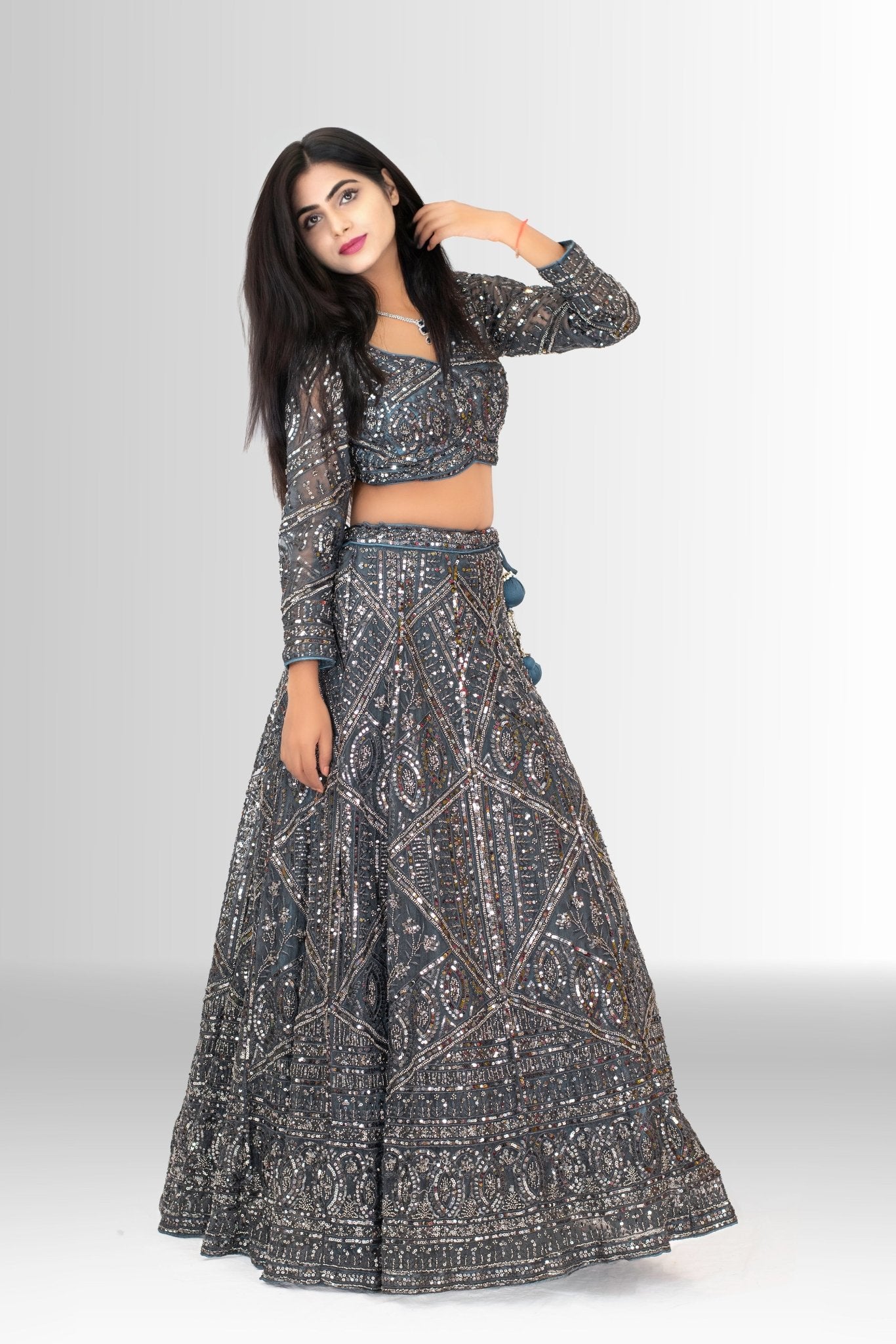 Model wearing a charcoal grey sequin lehenga choli by Rosio House, featuring a full-sleeve top and a sheer net dupatta with tassels.