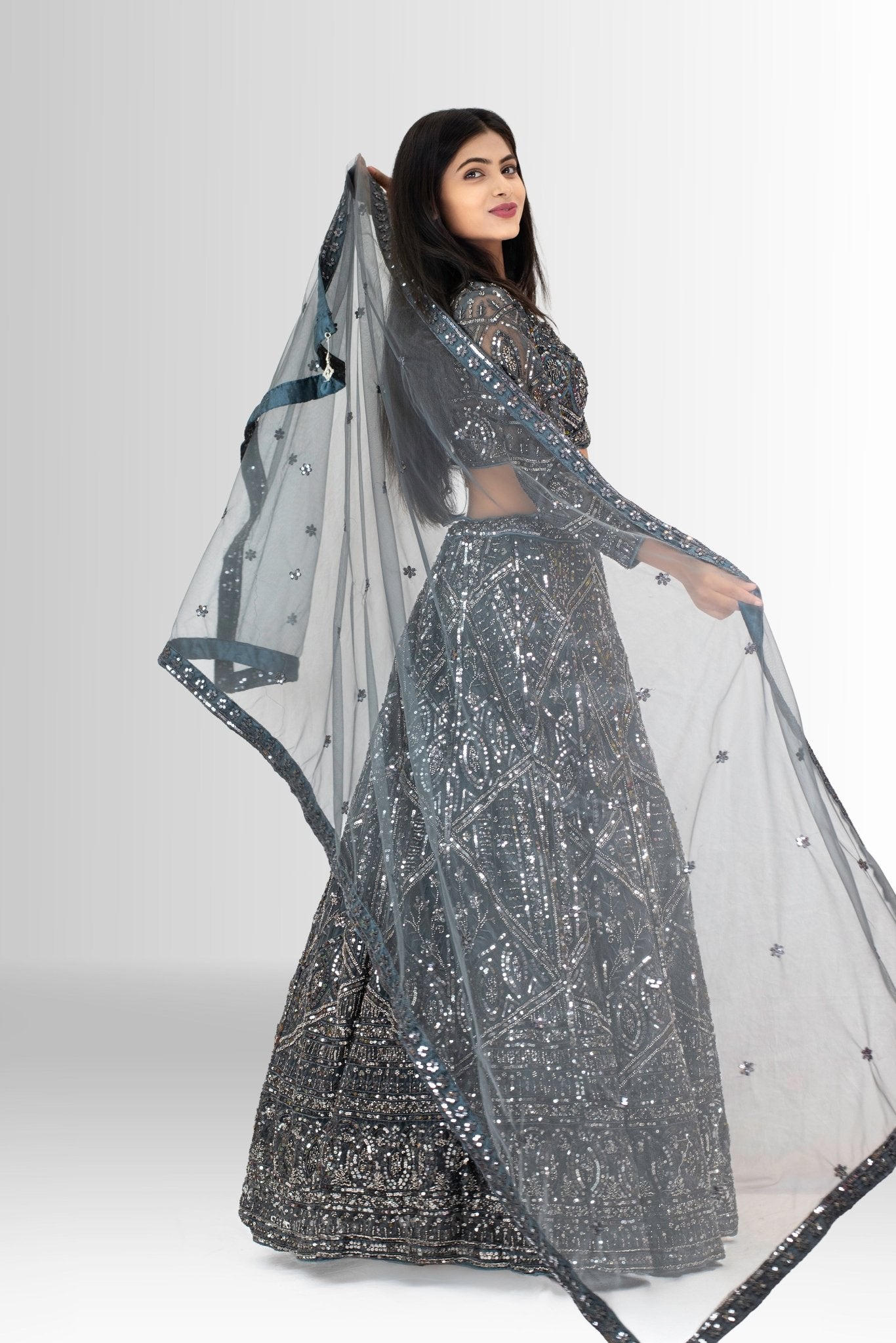 A smiling woman dressed in a glamorous grey designer lehenga, the perfect outfit for a modern Indian wedding reception or sangeet.