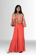 Model wearing a vibrant coral orange Indo western for women by Rosio House, featuring a crop top and an open-front jacket with detailed mirror work.