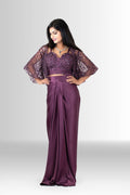 Model wearing Rosio House's wine-colored Indo-Western draped skirt set with a sequin bustier and embellished cape, posing against a grey studio background.