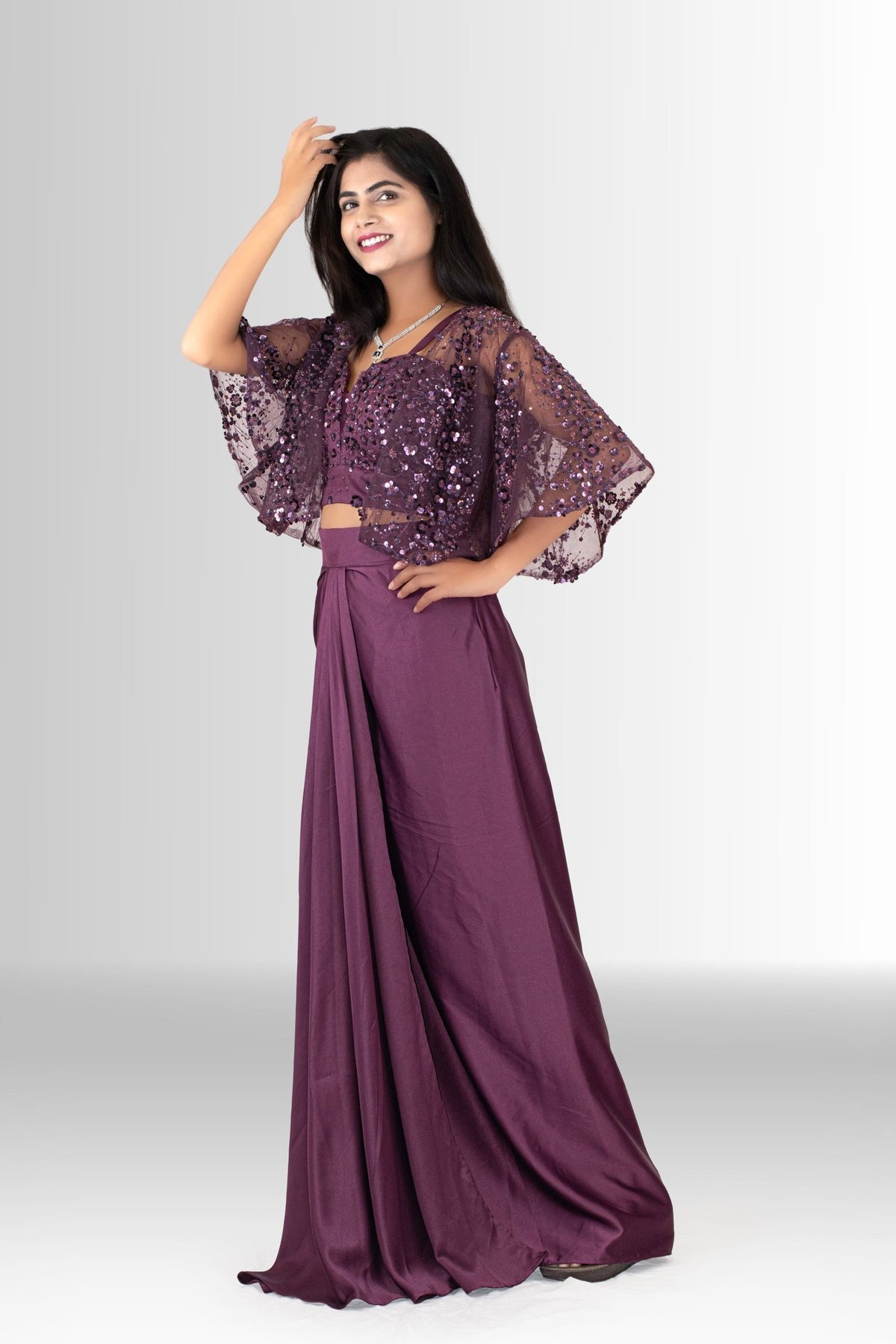 A woman twirling in a Rosio House wine-colored Indo-Western dress, showing the beautiful flow of the satin skirt and sheer flutter-sleeve cape.